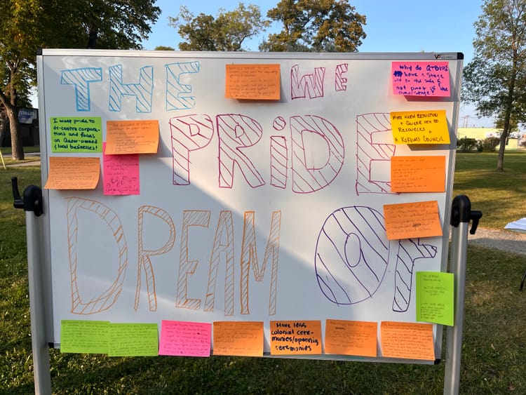 A whiteboard in a park with “The Pride we Dream Of” written on it, and notes affixed