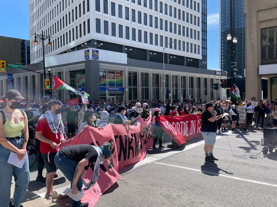 A group blocking the parade’s progress with banners, most wearing masks and many with keffiyehs